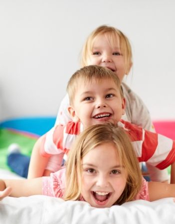 Image: three siblings laying on top of each other laughing